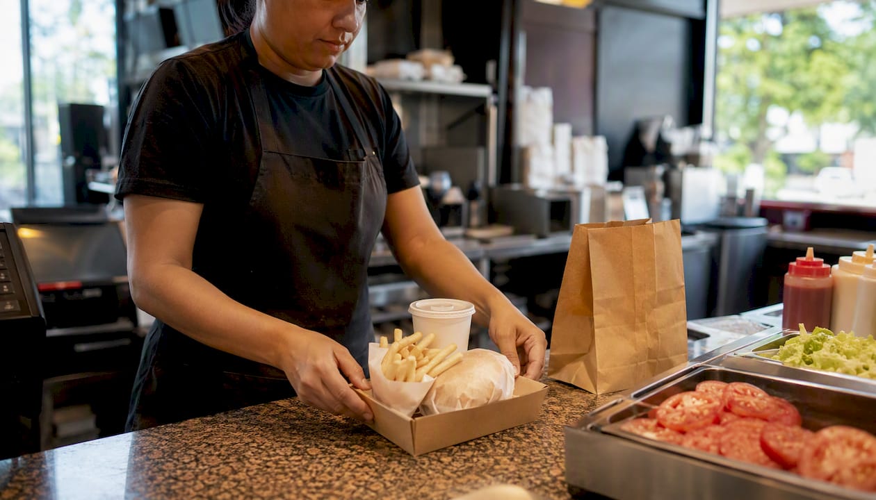Worker assembling value meal bundle in fast food kitchen